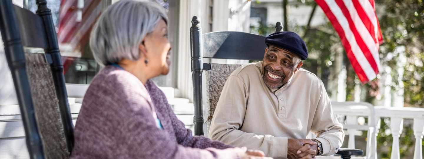 Two older adults laugh together while relaxing on their porch.