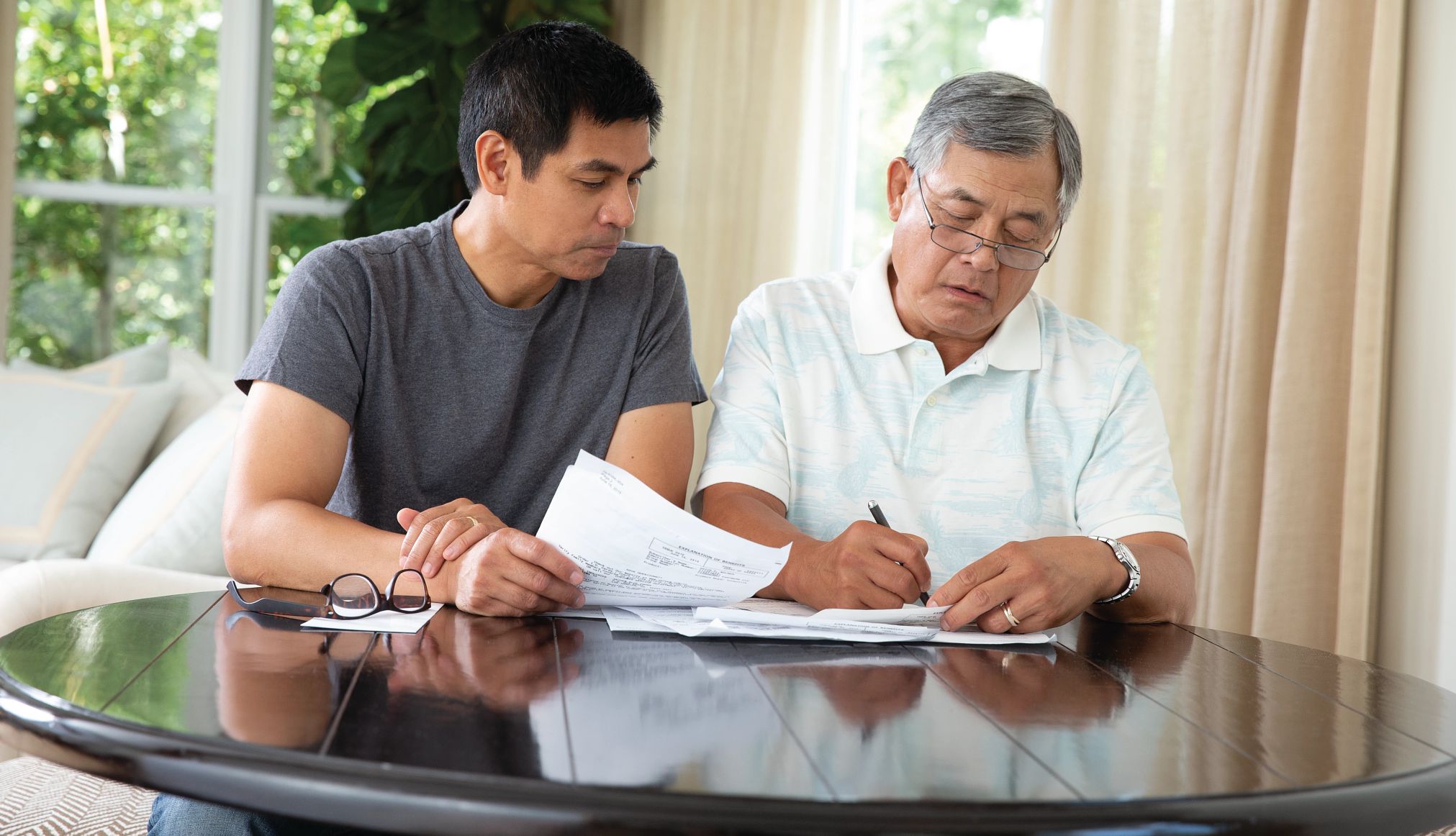 older parent and adult child sit at a table and fill out paperwork